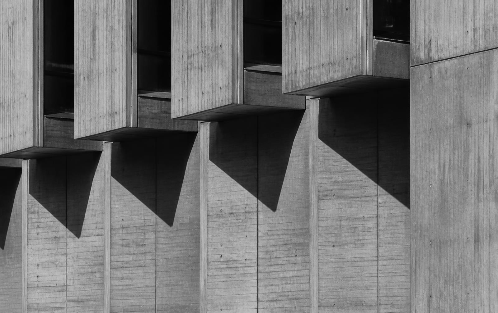 Board-formed brutalist concrete facade with repeating cantilevered window bays